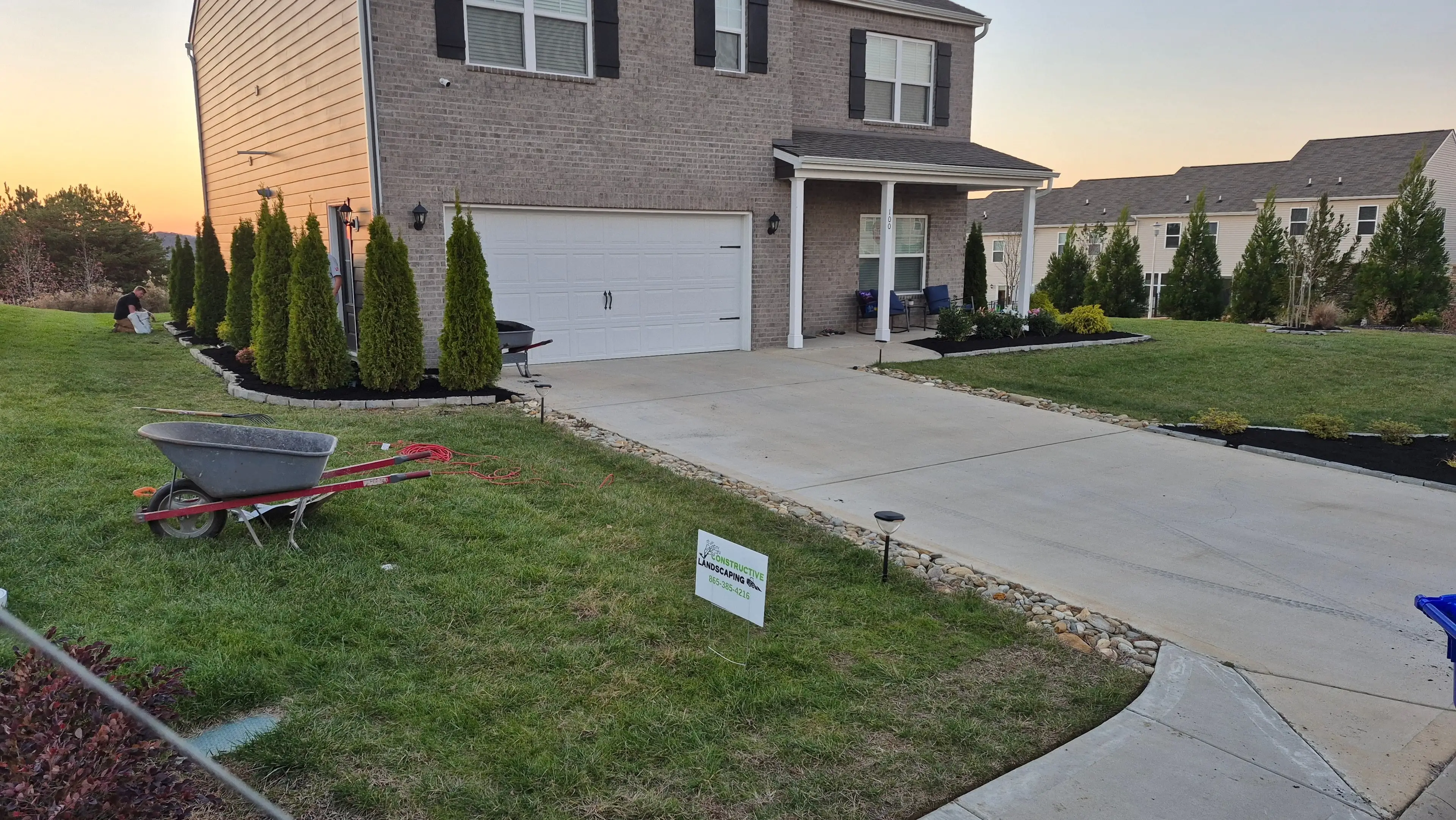 Front yard landscaping with mulch beds, arborvitae, and river rock at sunset