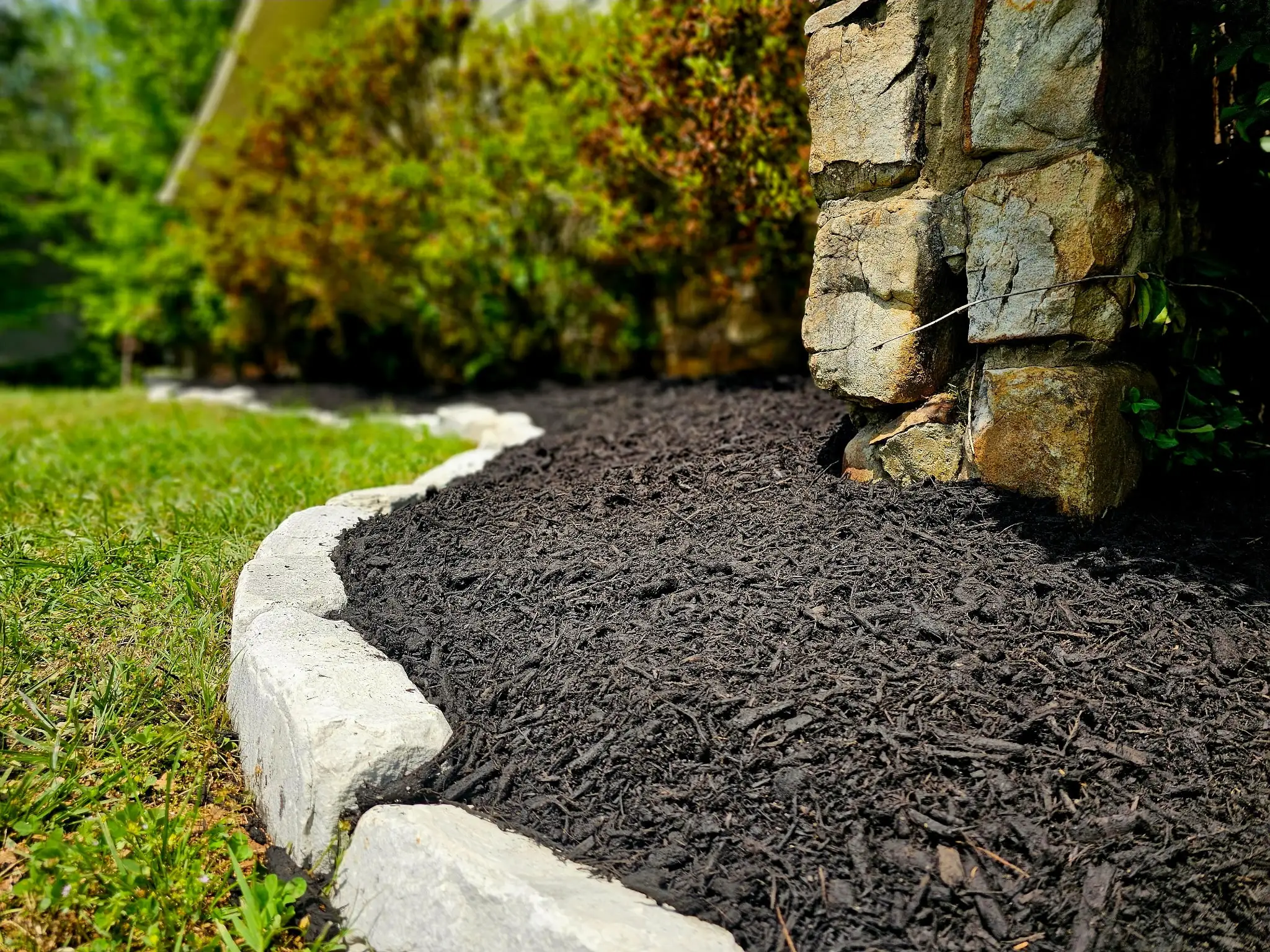 Close-up of stone edging with fresh black mulch bed at stone chimney base